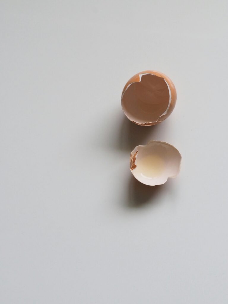 A top-down view of a broken eggshell on a minimalist white background, perfect for food and cooking concepts.